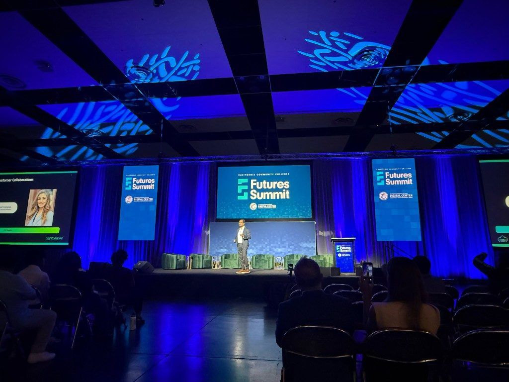 Wide view of the Futures Summit 2026 mainstage — Kiran Kodithala presenting, with a 'Customer Collaborations' slide on the side screen and the Futures Summit banner center-stage.